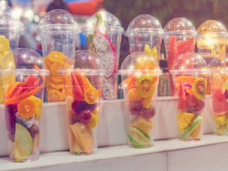 Pieces of various tropical fruits are in a plastic cocktail glass