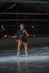 A young ice skater is holding her leg up in the air while she continues ice skating.