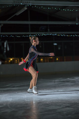 A young ice skater is slowly ice skating on the ice rink.