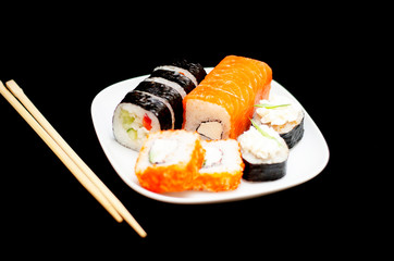 rolls with rice and fish on a white plate with wooden sticks on a black background