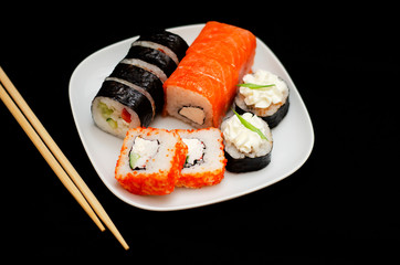 rolls with rice and fish on a white plate with wooden sticks on a black background