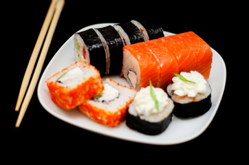 rolls with rice and fish on a white plate with wooden sticks on a black background