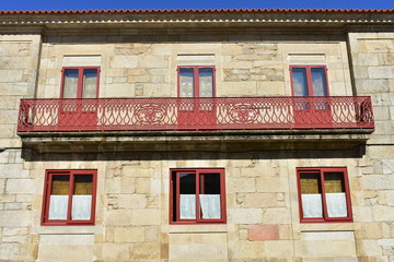 House with red iron handrail, stone walls and red wooden windows. Pontevedra, Galicia, Spain. Sunny day, blue sky.