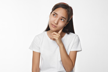 Thoughtful casually dressed young Korean female with black loose hair looking up with pensive...