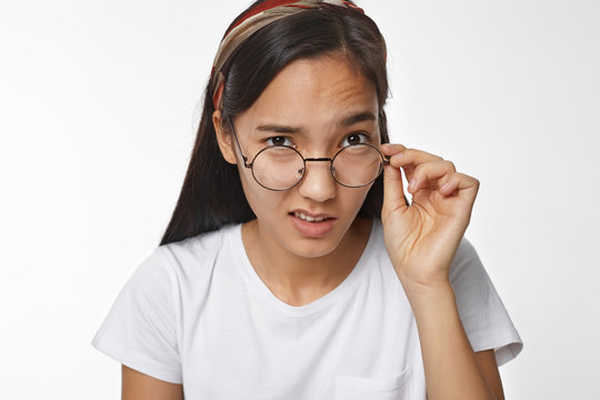 What did you say? Picture of black haired casually dressed strict young Korean female teacher lowering her round glasses and staring at camera with suspicious scrutinizing displeased facial expression