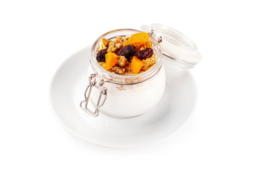 Closeup jar of creamy granola with nuts and dried fruits on a plate isolated at white background.