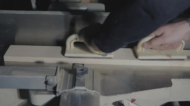 carpenter planes a piece of wood on a jointer