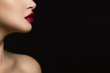 Naklejka premium Zbliżenie dolnej części twarzy kobiety o doskonałej skórze i pełnych ustach koloru marsala. Obraz na odosobnionym czarnym tle dodaje mu blasku.