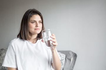 Beautiful charming woman drinking a big glass of water and wearing white clothes