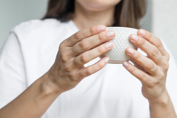 Nice and white cup of tea held up by woman's hands wearing white clothes 