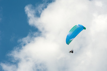 Alone paraglider flying in the blue sky against the background of clouds. Paragliding in the sky on a sunny day.