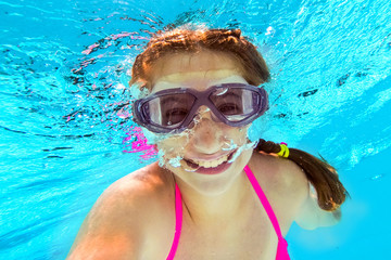 Naklejka premium Smiling little girl in swim goggles swimming underwater in pool. Teenage girl diving underwater