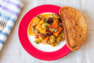 Caponata siciliana on a plate with toast close-up, top view