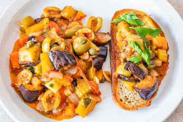 Caponata siciliana on a plate with toast close-up, top view