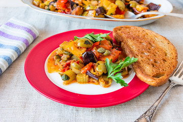 Caponata siciliana on a plate with toast close-up, top view