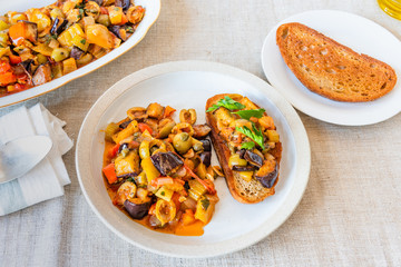 Caponata siciliana on a plate with toast close-up, top view