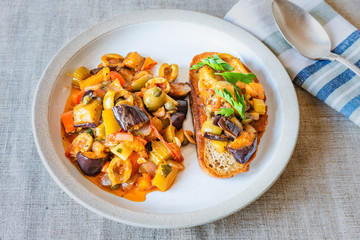 Caponata siciliana on a plate with toast close-up, top view