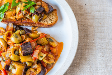 Caponata siciliana on a plate with toast close-up, top view, copy space for recipe