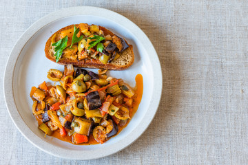Caponata siciliana on a plate with toast close-up, top view, copy space for recipe