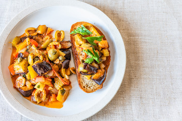 Caponata siciliana on a plate with toast close-up, top view, copy space for recipe