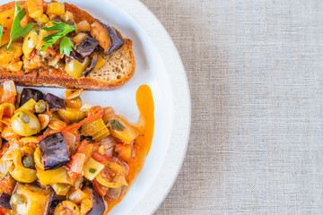 Caponata siciliana on a plate with toast close-up, top view, copy space for recipe