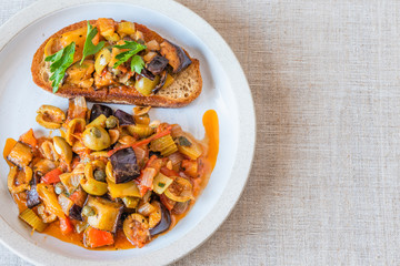 Caponata siciliana on a plate with toast close-up, top view, copy space for recipe