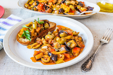 Caponata siciliana on a plate with toast close-up on a rustic background