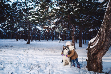 Fototapeta na wymiar Funny little girl hugging her big Malamute dog in winter in the forest.