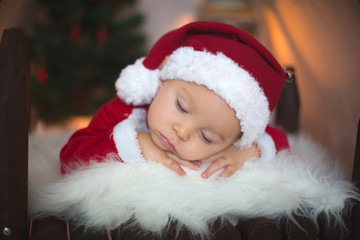 Fototapeta na wymiar Adorable little toddler baby boy dressed in canta claus costume, sleeping in baby bed in front of crhistmas teepee