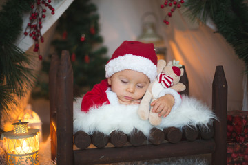 Adorable little toddler baby boy dressed in canta claus costume, sleeping in baby bed in front of...