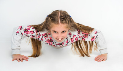 Little blonde girl doing push-ups and smiling on light background