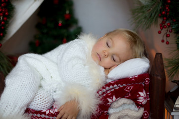 Adorable little toddler baby boy dressed in canta claus costume, sleeping in baby bed in front of...