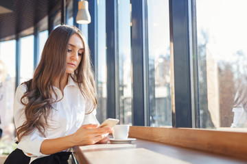 Young beautiful woman in business clothes use smartphone in a cafe
