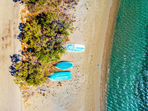 Three small rowing boats laying upside down on a beach by the sea, Paros island, Greece
