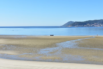 Beach with wet sand, clear blue water and a boat. Small coastal village, Galicia, Spain. Sunny day, blue sky.