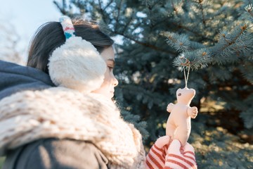 Winter outdoor portrait of child girl near the Christmas tree, smiling girl decorates Christmas tree with toy, golden hour