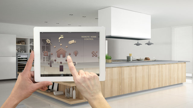 Smart remote home control system on a digital tablet. Device with app icons. Interior of professional modern wooden kitchen with accessories in the background, architecture design