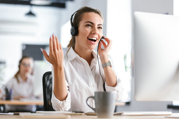 Emotional business woman in office callcenter working with computer wearing headphones.