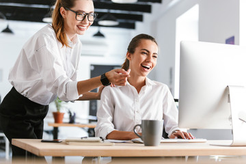 Happy cheerful colleagues business women in office working while using computer.