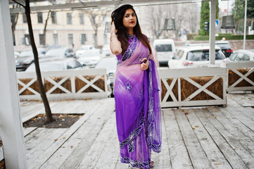 Indian hindu girl at traditional violet saree posed at street against wooden terrace.