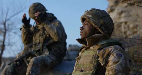 Medium slow motion shot of fully equipped and armed african american soldier lost in thought while taking a break