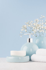 Delicate elegant ceramic decorations for bathroom - soft blue bowls, vase, white flowers, towel and soap on white wood table. Modern bath interior, vertical.