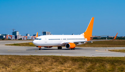 Huge shiny white-orange passenger airplane at the runway on the background of modern city