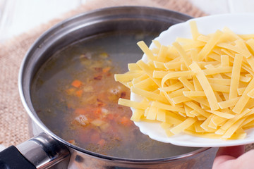 The cook adds macaroni to the soup