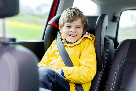 Adorable Cute Preschool Kid Boy Sitting In Car In Yellow Rain Coat. Little School Child In Safety Car Seat With Belt Enjoying Trip And Jorney. Safe Travel With Kids And Traffic Laws Concept