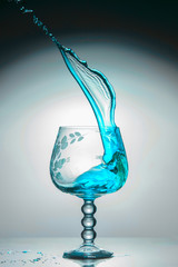 Transparent glass with a blue jet of liquid up, close-up