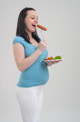 Pregnant woman with a plateful of salad and sausage on a grey background
