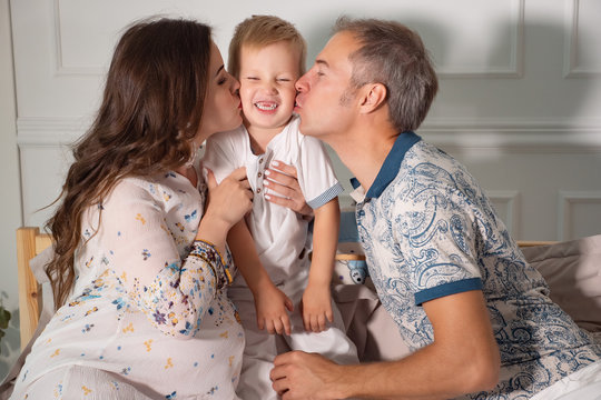 Happy parents kissing little boy in bed