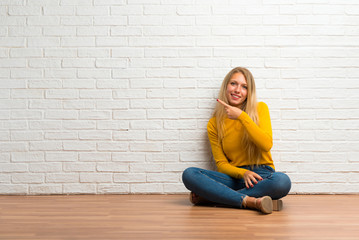 Young girl sitting on the floor pointing to the side with a finger to present a product