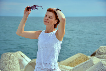 A woman in a long white dress stands on the beach by the water and looks into the distance